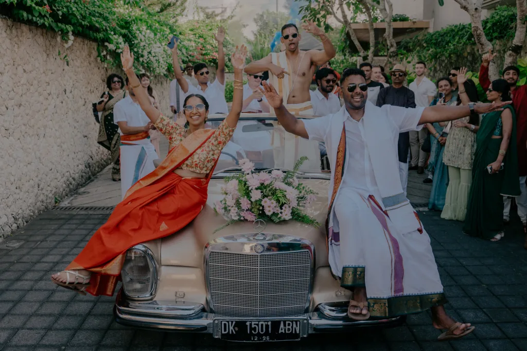 The groom's baraat procession arriving on a vintage car, family dancing alongside