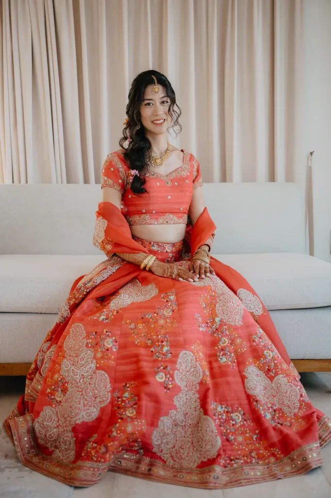 The bride in a coral and gold lehenga before the ceremony