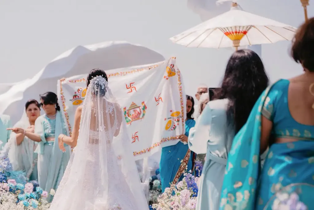 The bride walking in beneath a hand-held cloth canopy