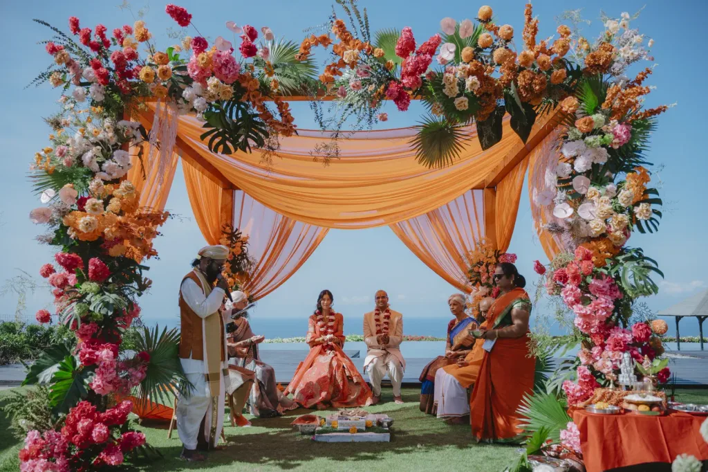 Wide view of the ceremony mandap, drenched in orange and pink florals above the cliff
