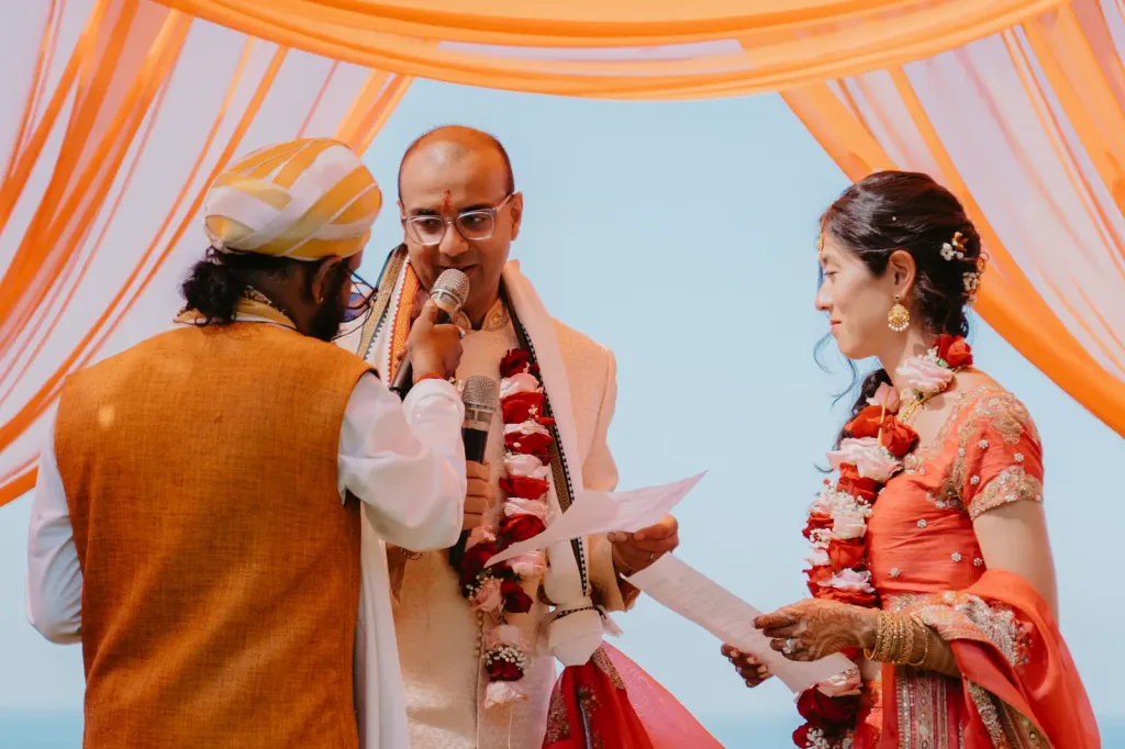 The couple exchanging vows under the mandap with the priest and their families