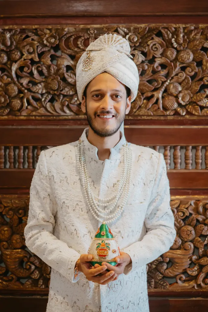 Portrait of the groom in ivory sherwani against a carved Balinese door