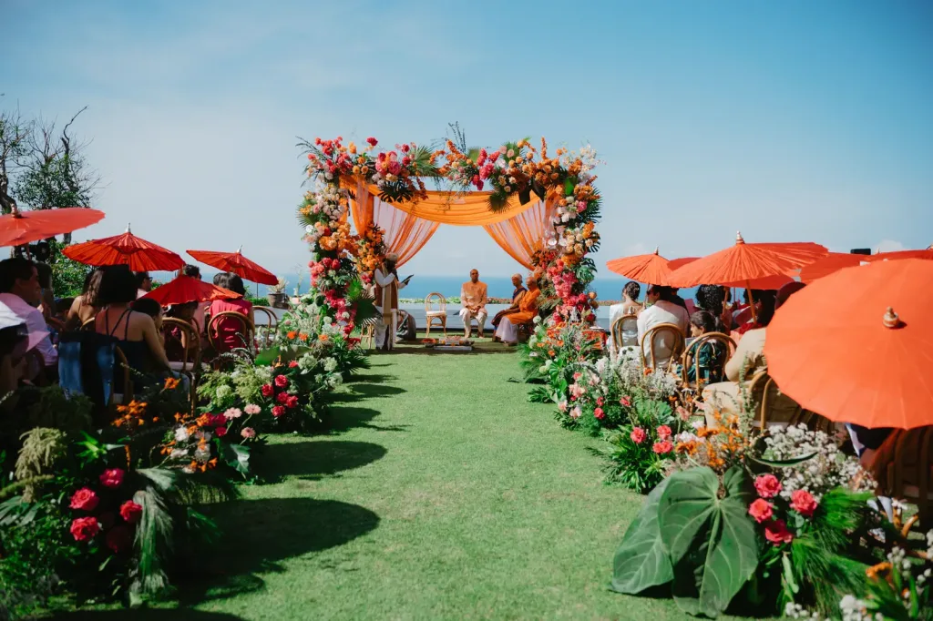 Guests seated under orange parasols on the ceremony lawn above the sea