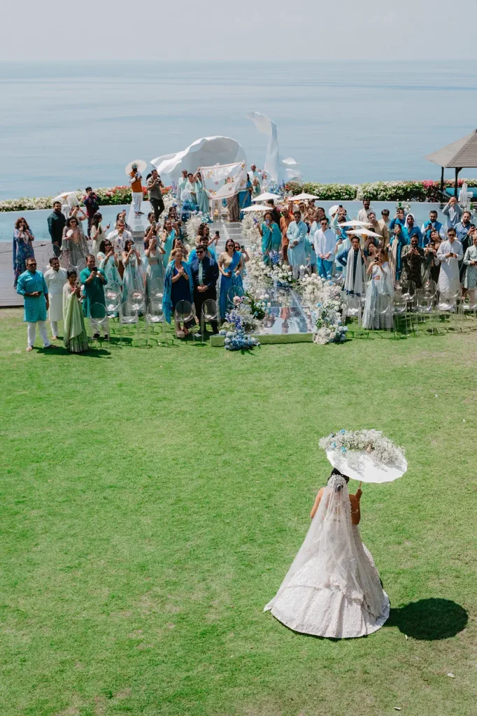 The ceremony from the back of the lawn, guests in pastels, the ocean beyond