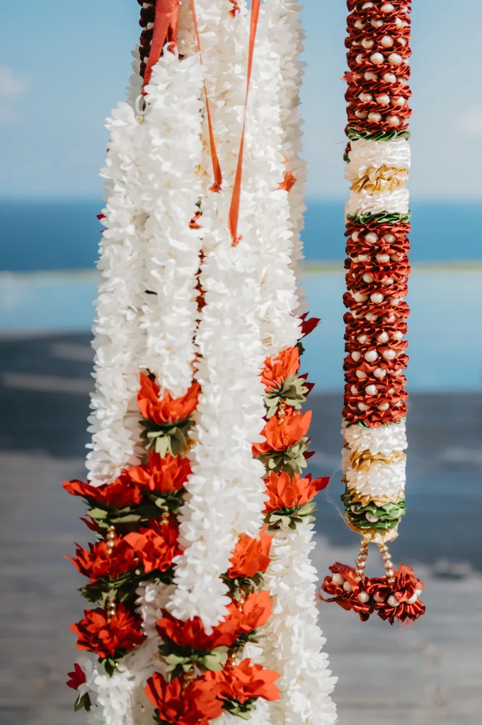 Two varmala garlands of white and orange flowers hanging against the sea