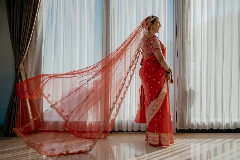 A bride in a red saree with the drape fanned out behind her