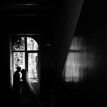 Monochrome view of the silhouette of wedding couple which is nearly kissing near the window
